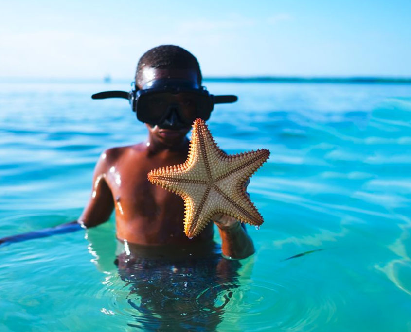 Bambino con stella marina in Oceano Indiano Bambino con stella marina in Oceano Indiano
